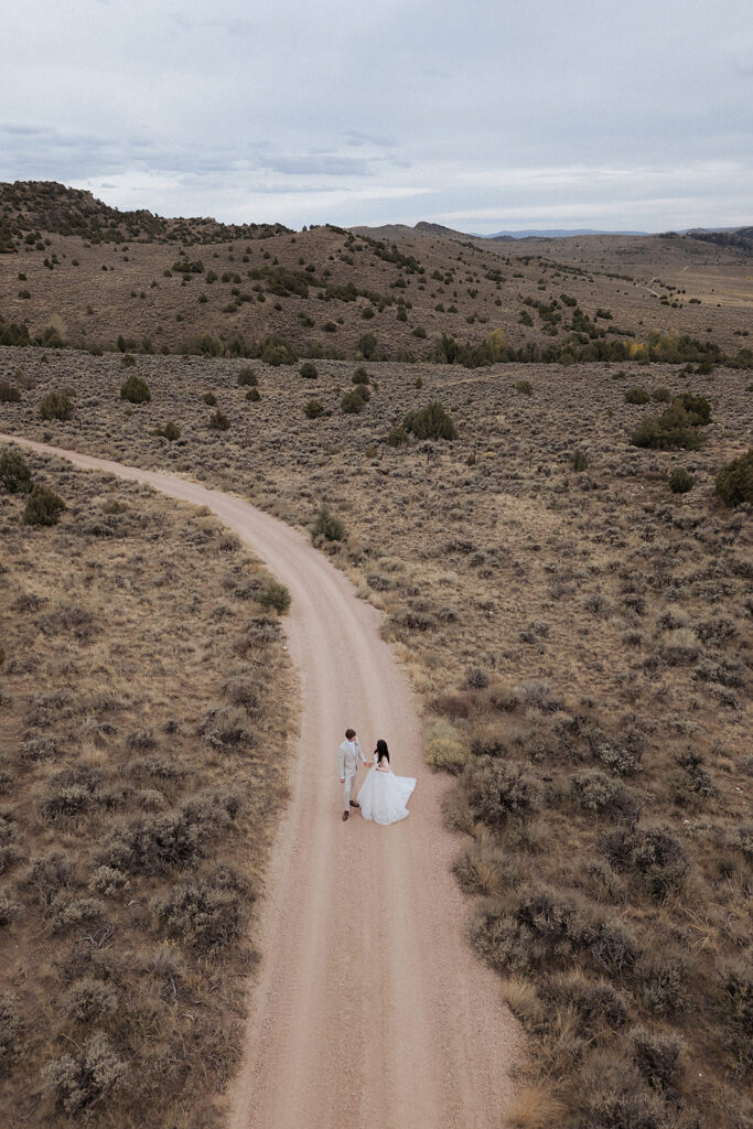 Drone shot of newlyweds on dirt road through Brush Creek Ranch
